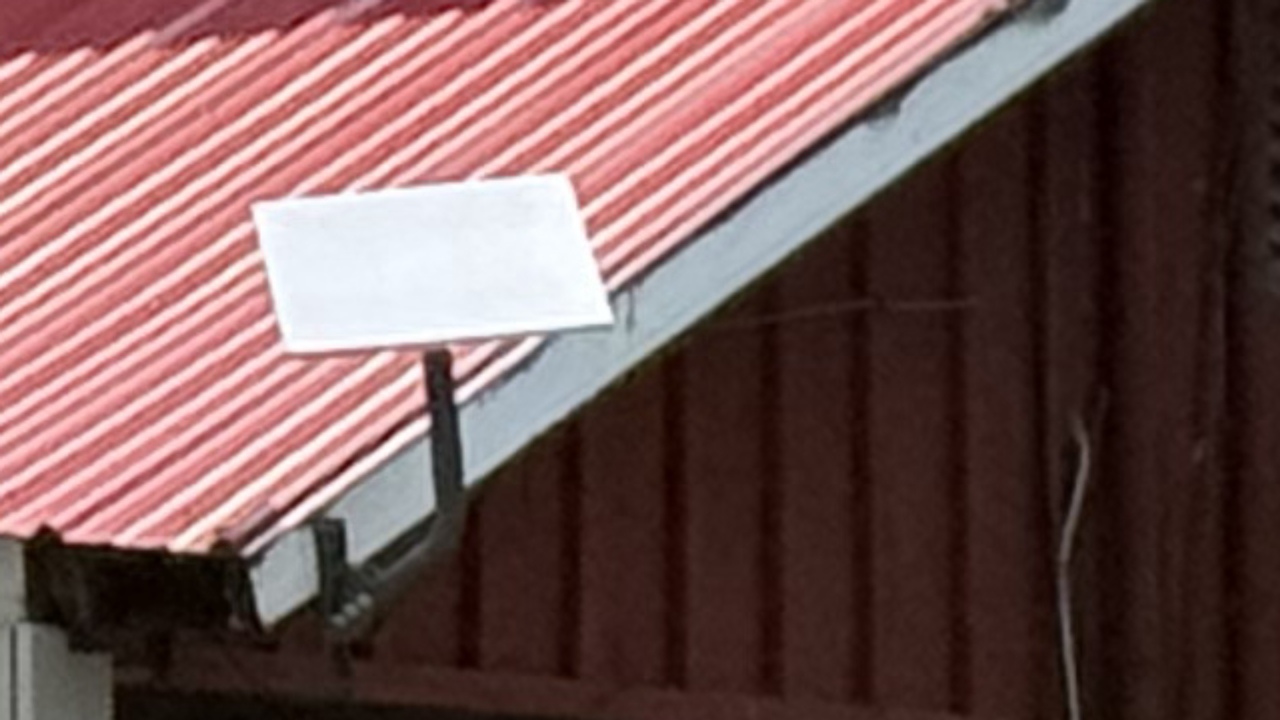 Starlink flat-panel dish mounted on a pole bracket at the roof edge of Tommy Guns Pizzeria in Warrensburg, NY, above the red metal roof.